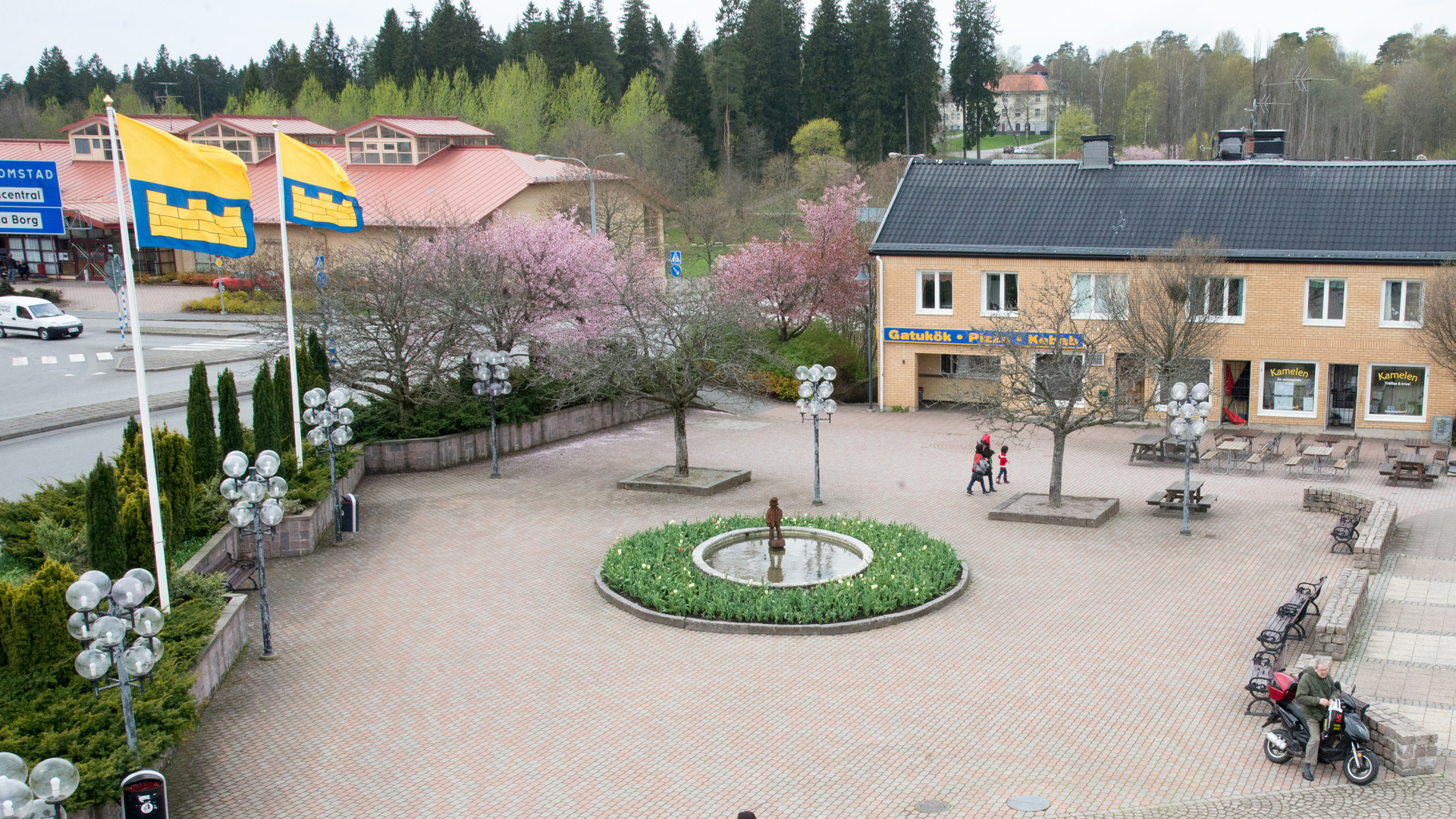 torg med en fontän i mitten, runt fontänen finns det en blomsterrabatt till vänster kant på bilden finns det två flaggstänger som har Sävsjö kommuns flaggor hissade