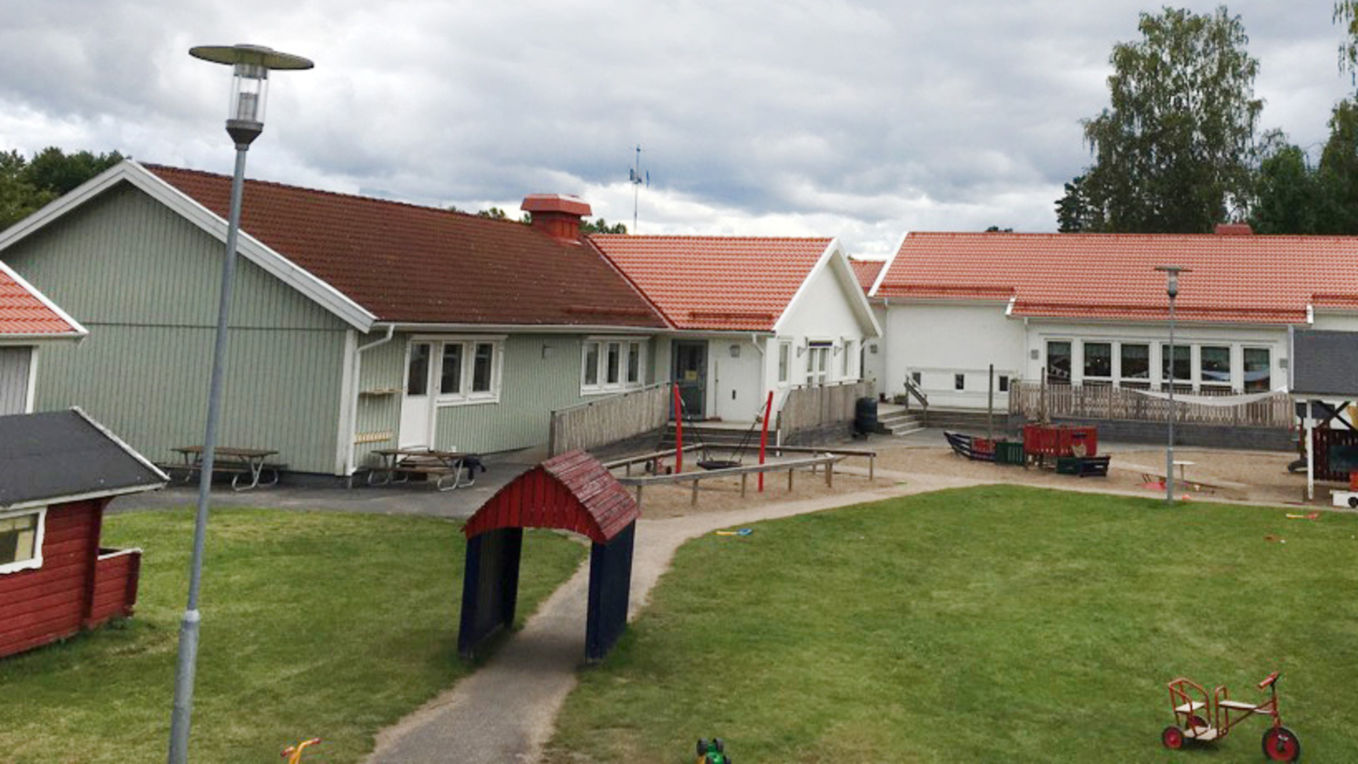 Bild på Förskolan Paletten som består av tre vita trähus med röda tak. Lekplats finns framför.